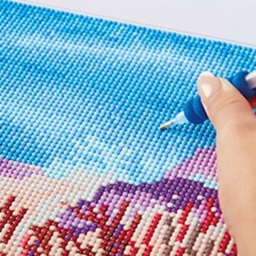 Zoomed in hand working on diamond dots art focusing on a large blue area.